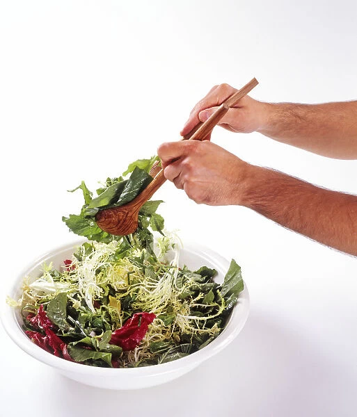 Mans hands using salad servers to toss salad leaves