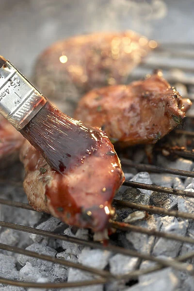 Meat on barbecue grill being glazed with paint brush