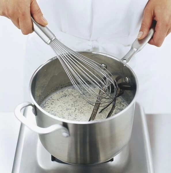 Metal whisk being used to stir milk and vanilla pods in saucepan, high angle view