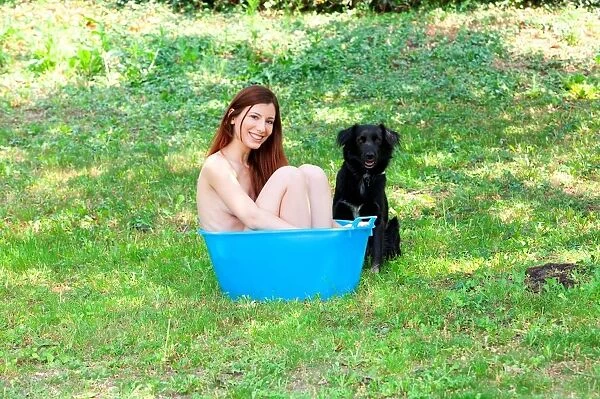 A Naked Woman Smiling in the Garden in a Bucket Blue with a Black Dog