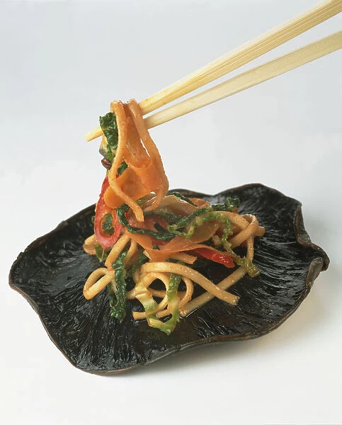 Noodles and vegetables on top of a large field mushroom, being picked up with chopstick