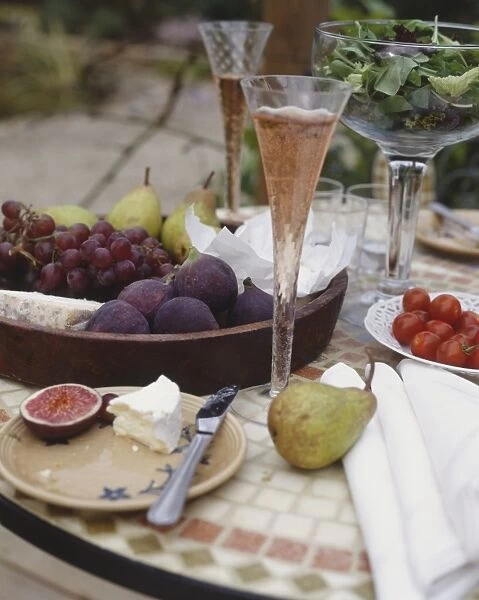 Ornate table with flutes of bubbly liquid, and bowl of figs, pears, grapes and cheese