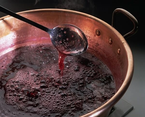 A pan containing liquid, boiling jam, and a spoon