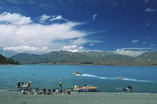 People sitting on the banks of Lake Tekapo, South Island, New Zealand, a popular venue for water sports, including speed boats