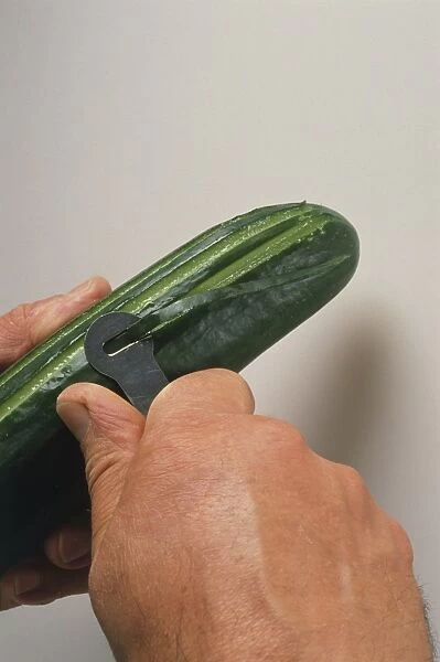 Person peeling cucumber with peeler, close-up