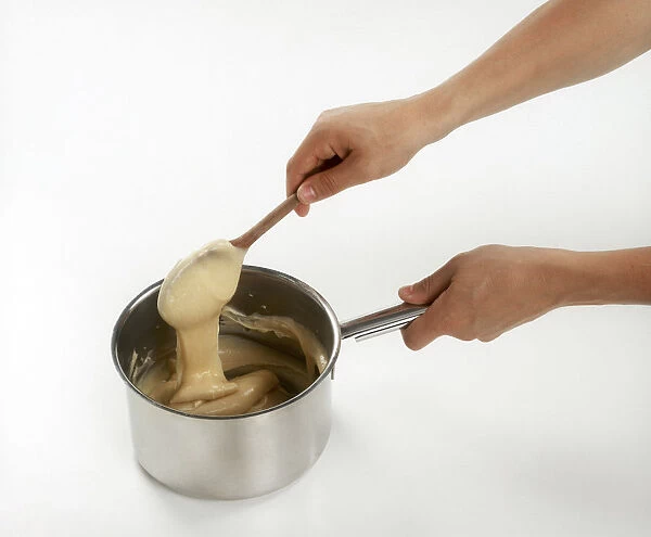 Person using wooden spoon to stir batter in saucepan, close-up