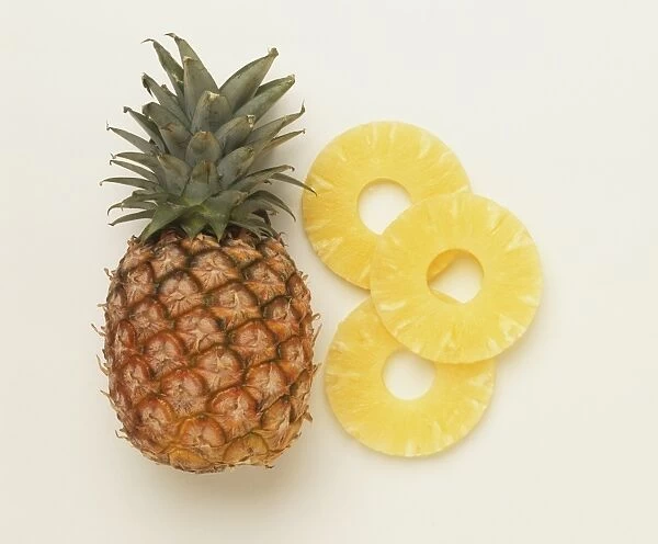 Whole pineapple and three pineapple rings, front view