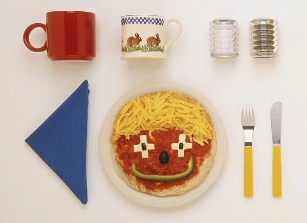 Pizza decorated as a smiley face, blue napkin, salt and pepper shakers, two mugs, knife and fork