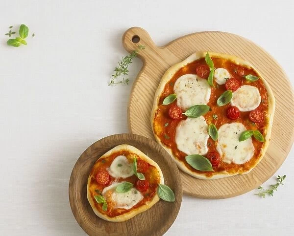 Two pizzas topped with mozzarella cheese, cherry tomatoes, basil and thyme leaves