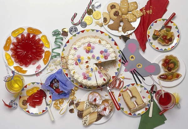 Plate of cakes, biscuits and jelly beans, with sweets and party decorations scattered