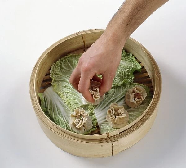 Positioning uncooked open-faced dumplings (Shao Mai) on top of Chinese cabbage leaves in bamboo steamer