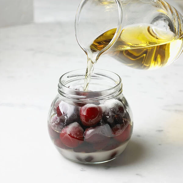 Pouring brandy over cherries in jar, close-up