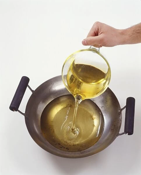 Pouring oil into a wok from a glass jug, view from above