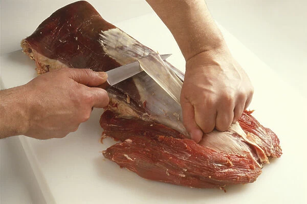 Pulling away white membrane from beef tenderloin, using knife, close-up