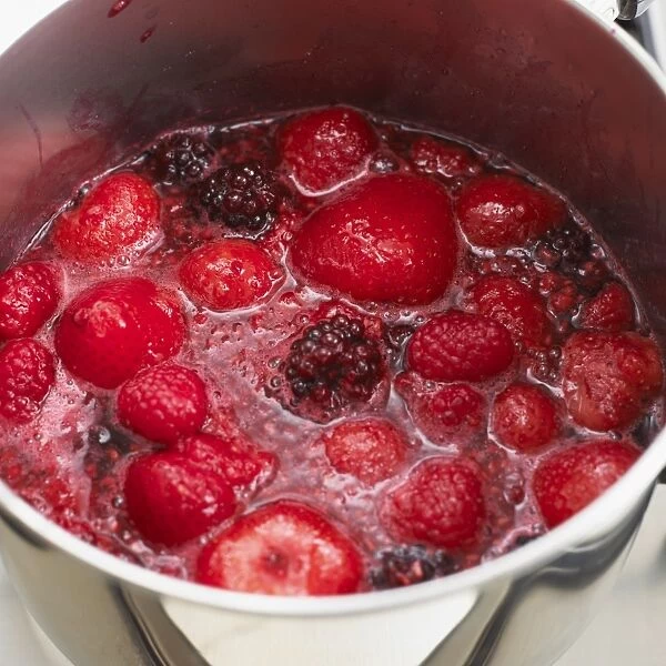 Raspberries and strawberries boiling in saucepan