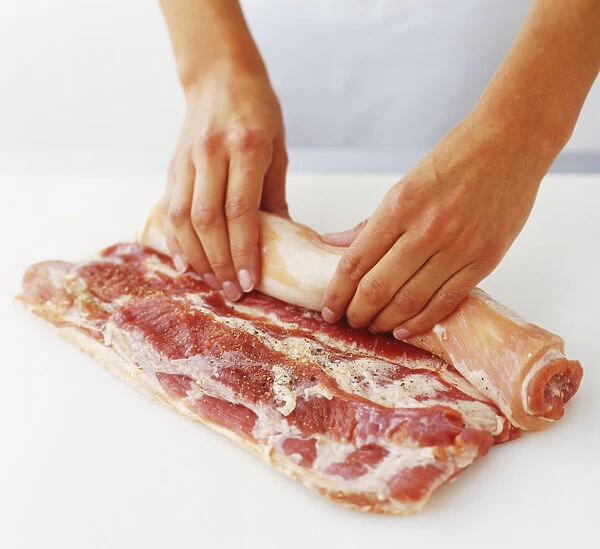 Raw belly of pork being rolled in preparation for braising, high angle view