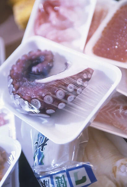 Raw octopus tentacle wrapped in plastic, displayed for sale with similarly packaged