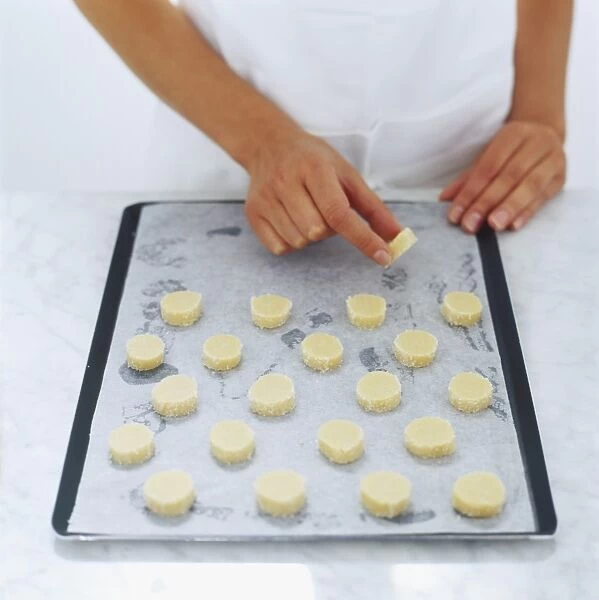Raw shortbread biscuits being laid on baking tray, high angle view