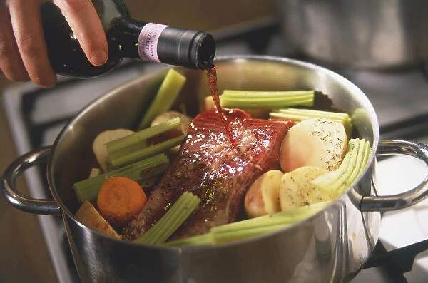 Red wine pouring out of bottle onto raw red meat and vegetables in a casserole (beef daube)