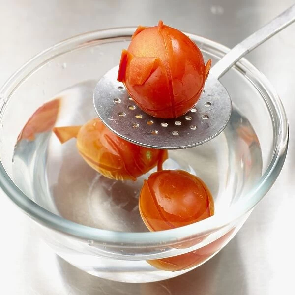 Removing blanched tomato from bowl of hot water using spatula
