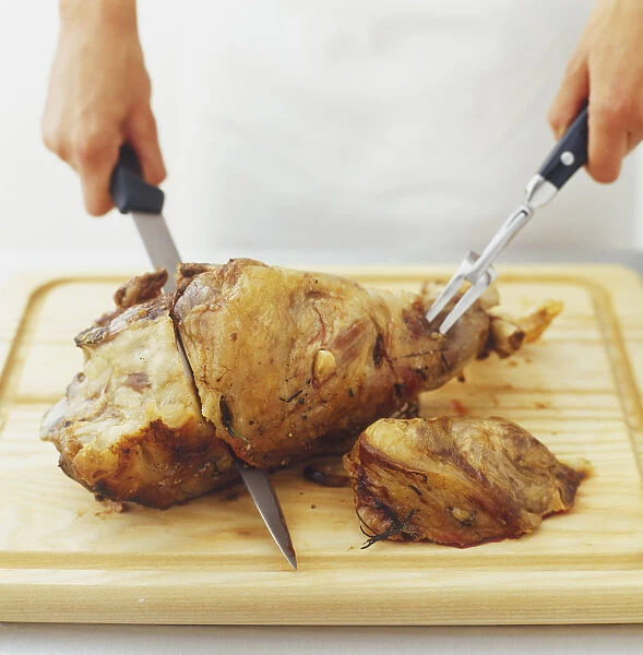 Roast lamb being sliced with knife and carving fork, side view