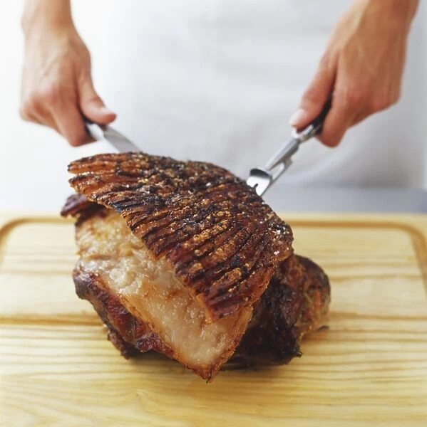 Roast shoulder of pork being sliced with knife and carving fork, side view