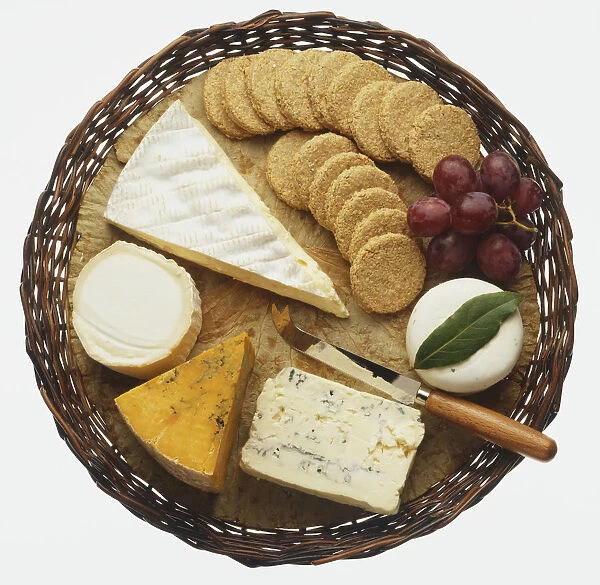 Selection of cheeses, oat biscuits and red grapes, served on a wicker tray, view from above