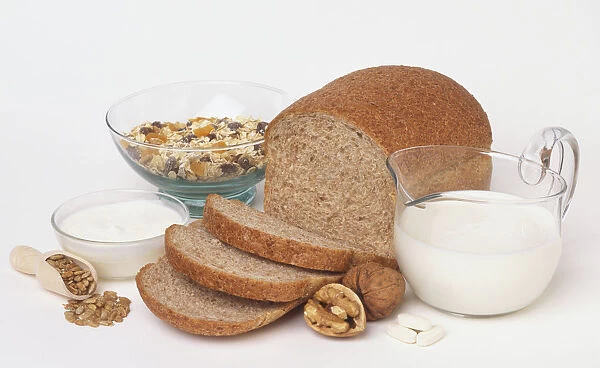 Selection of foods rich in magnesium, including a jug of milk, wholemeal brown bread, muesli, yoghurt, walnuts and grains, side view