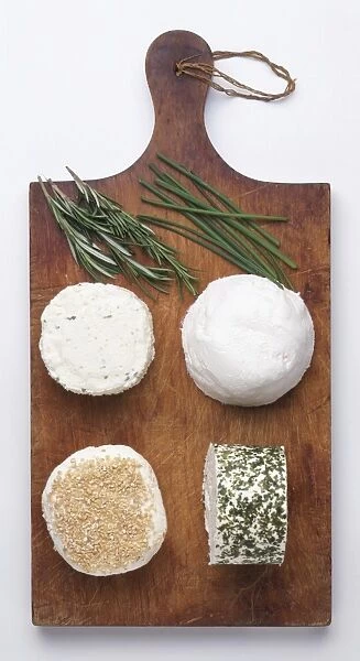 A selection of soft cheeses and herbs on chopping board, cows milk cheese with garlic, ewes milk cheese with nuts, ewes milk cheese rolled in herbs and goats cheese