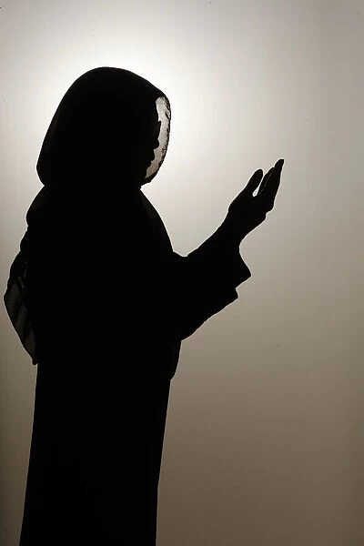 Silhouette of muslim woman in abaya prays with her hands up in air