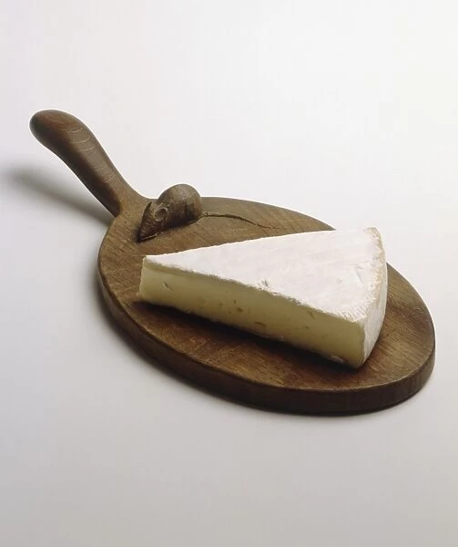 Slice of Brie on circular wooden chopping board with handle, elevated view