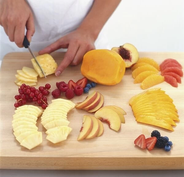 Slicing a selection of fresh fruit on a wooden chopping board, high angle view