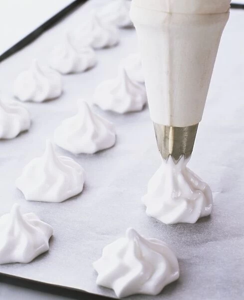 Small vanilla meringues being piped onto a baking sheet