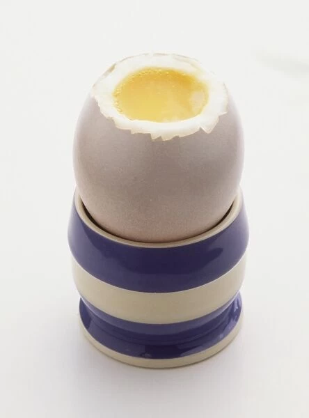 Soft boiled egg with top off, in blue and white striped egg cup