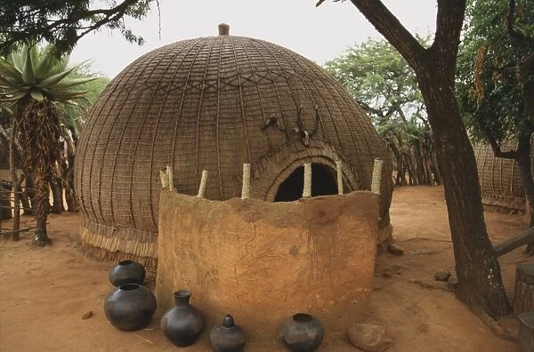 South Africa, pots and a leather hide screen in front of a hut built from a wooden framework covered with plaited grass or rushes