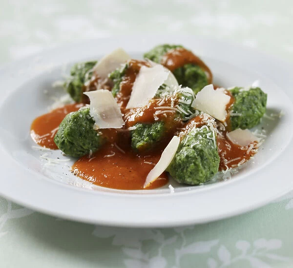 Spinach gnocchi with tomato sauce and parmesan shavings, on a plate