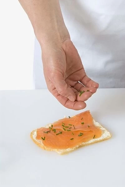 Sprinkling chives onto a smoked salmon and cream cheese sandwich
