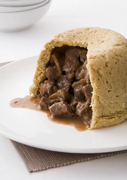 Steak and kidney pudding with stuffing showing, on a plate, close-up