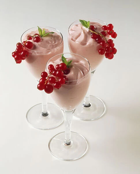 Three stemmed glasses full of a redcurrant cream dessert, all of which are decorated with redcurrants