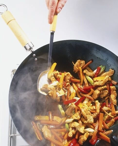 Stir-fried chicken with red peppers, yellow peppers, carrots and spring onions in a wok
