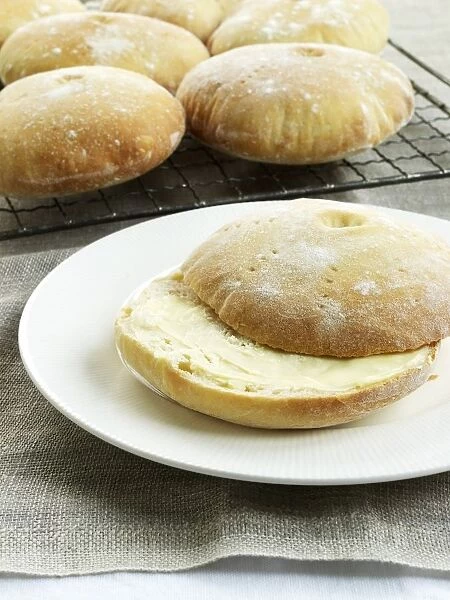 Stottie cakes, buttered on plate and on cooling rack nearby, a type of bread originally from Newcastle, Northeast England, close-up