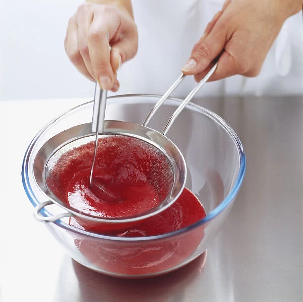 Straining raspberry puree into glass bowl through seive