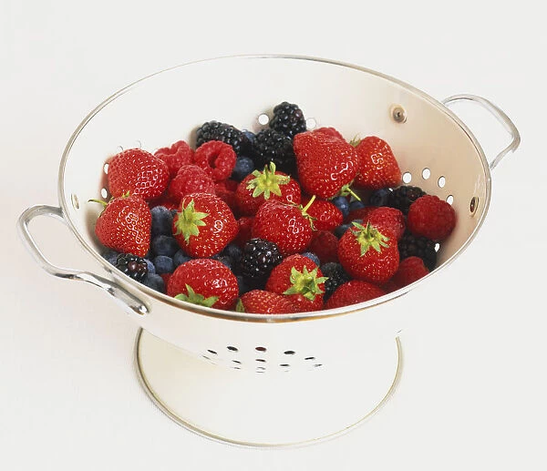 Strawberries, blackcurrents, blackberries and blueberries in a white metal colander, close up