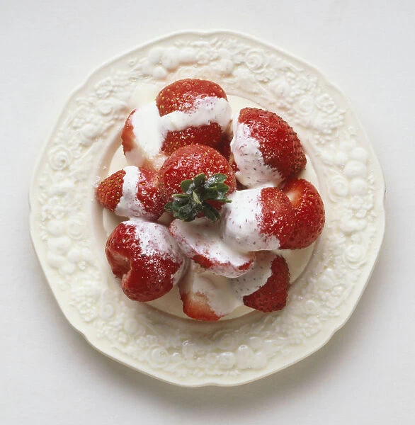 Strawberries topped with cream on a plate, view from above