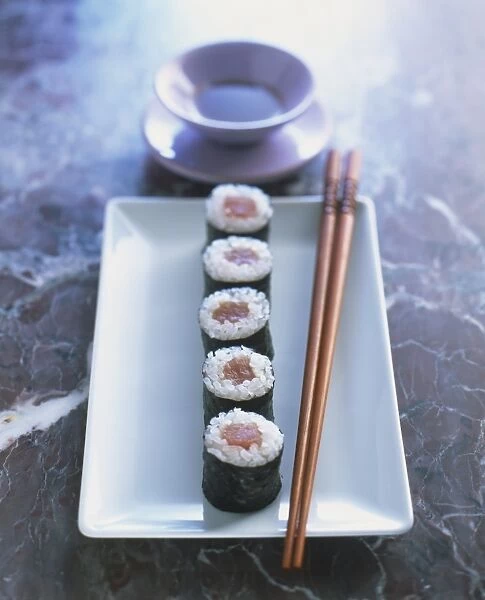 Five sushi parcels on rectangular plate with chopsticks, small sauce bowl, close up