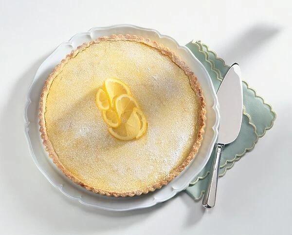 Tarte au Citron topped with lemon twists and icing sugar, served on white plate, with napkin and dessert knife
