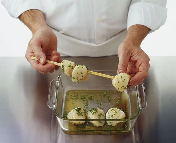 Threading herb-flavoured scallops onto a wooden skewer