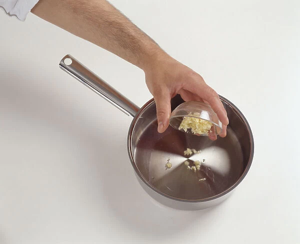 Tipping chopped garlic from glass bowl into saucepan