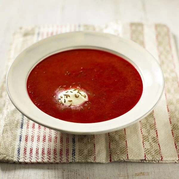 Tomato borscht served in soup bowl with sour cream and cumin seeds