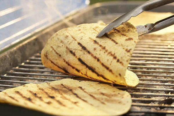 Tortillas on barbecue grill, being turned with tongs
